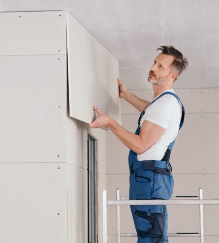 Builder or handyman fitting wall cladding inside a new build house standing on low metal scaffolding